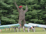 A 19-foot-tall arboreal sculpture situated next to seven canoes with murals painted on them.