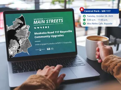 Person sitting at a café table with coffee and laptop showing a presentation about the Muskoka Road 117 Main Streets project; event details for a drop-in session at Miss Nelle’s Café are displayed beside them