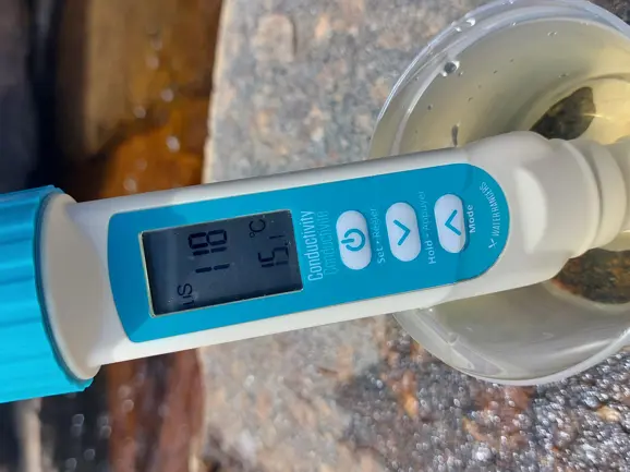A handheld conductivity meter in a water sample.